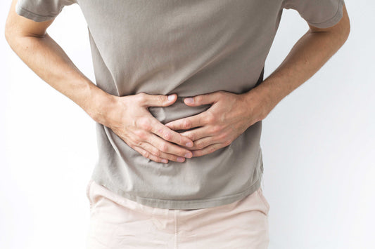 Person holding their stomach, possibly indicating discomfort or pain, on a plain background