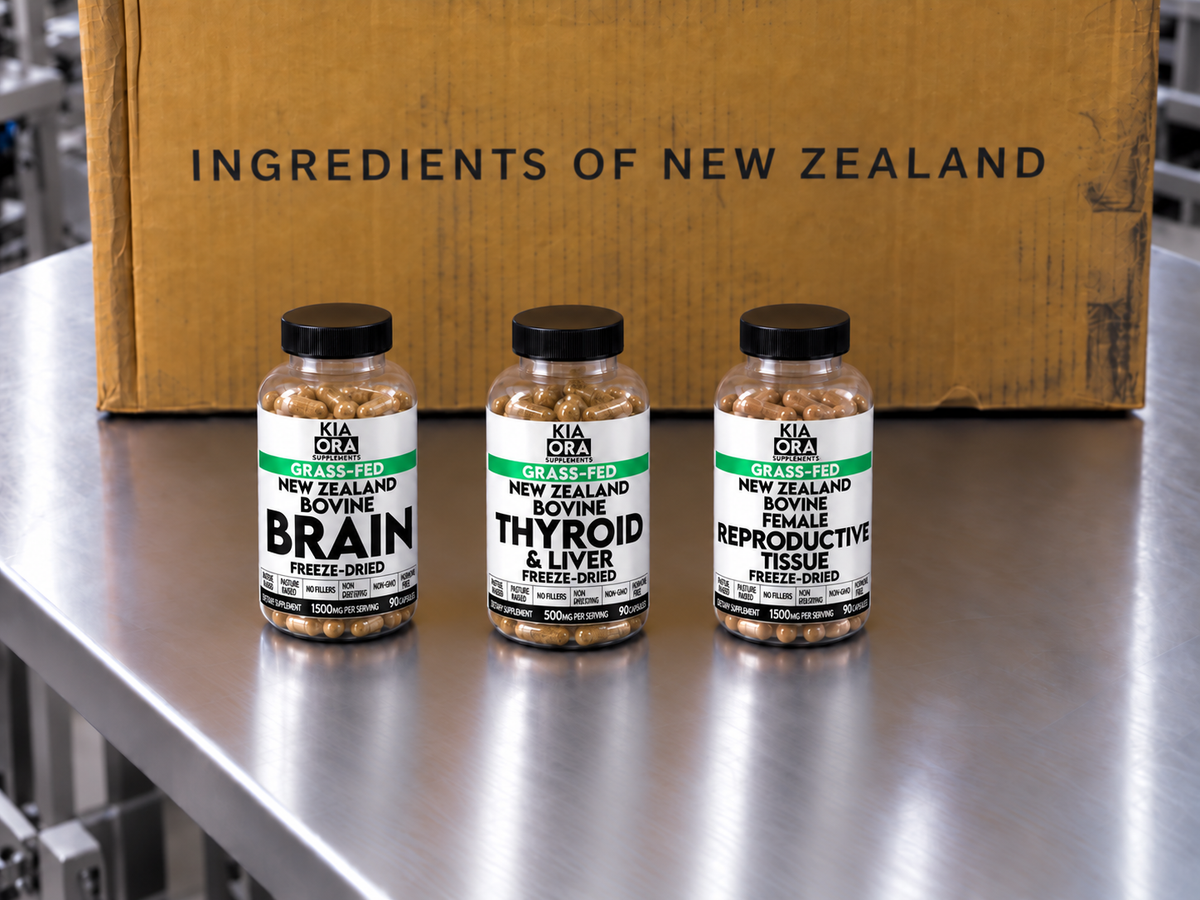 Three supplement bottles labeled Kia Ora Grass-Fed New Zealand Bovine Brain, Thyroid & Liver, and Reproductive Tissue Freeze-Dried, arranged on a stainless steel surface in front of a cardboard box with the text 'INGREDIENTS OF NEW ZEALAND'.