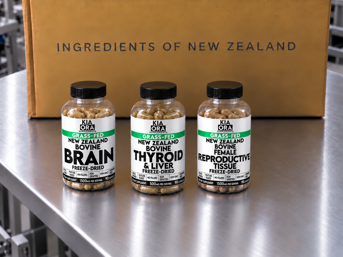 Three supplement bottles labeled Kia Ora Grass-Fed New Zealand Bovine Brain, Thyroid & Liver, and Reproductive Tissue Freeze-Dried, arranged on a stainless steel surface in front of a cardboard box with the text 'INGREDIENTS OF NEW ZEALAND'.